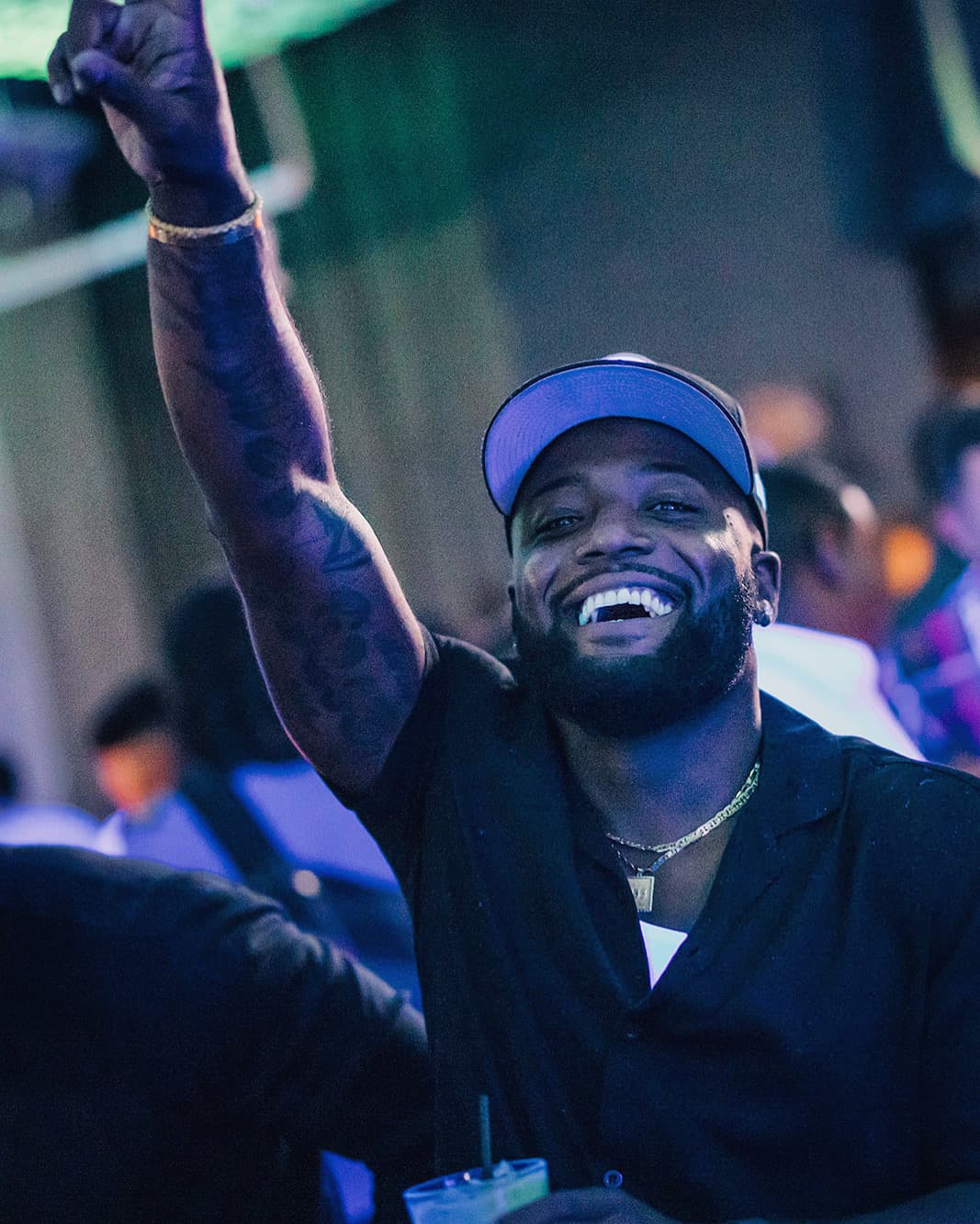 Smiling bearded man in a baseball cap raises his arm at a lively night event.