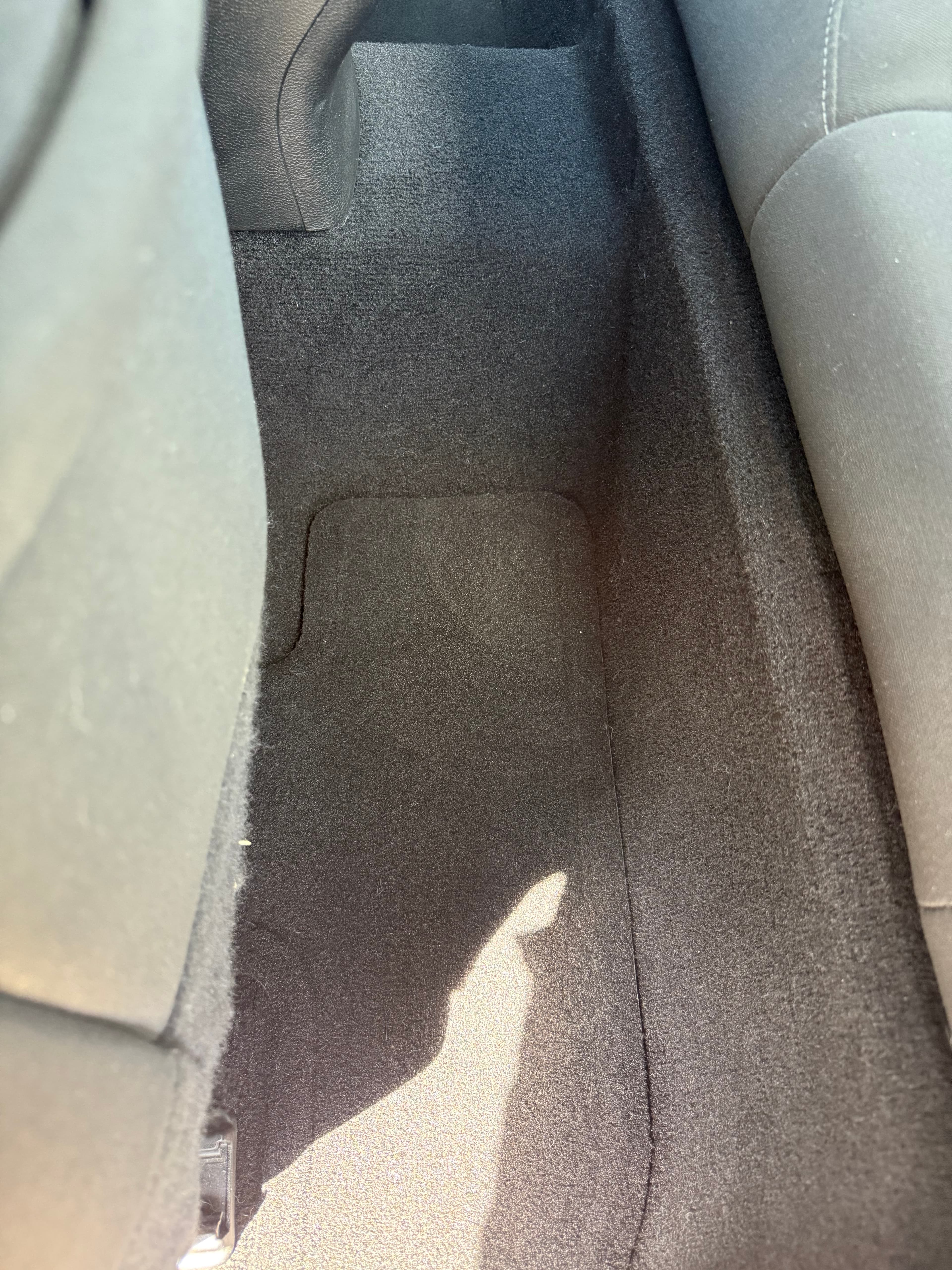 Dark grey car floor carpet and mat between two fabric seats with bright sunlight.