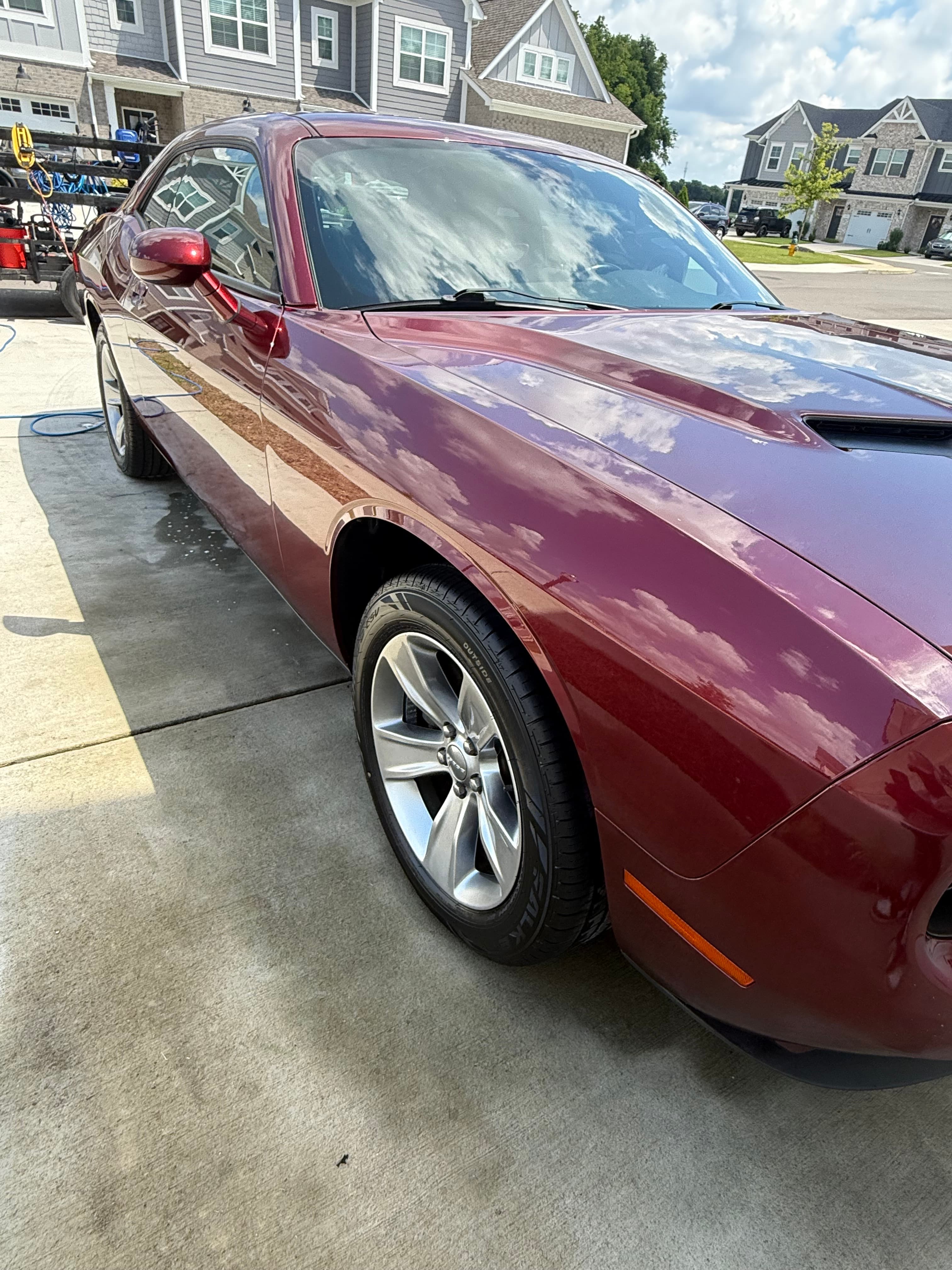 Maroon car front fender and silver wheel reflecting a cloudy sky on a concrete driveway.