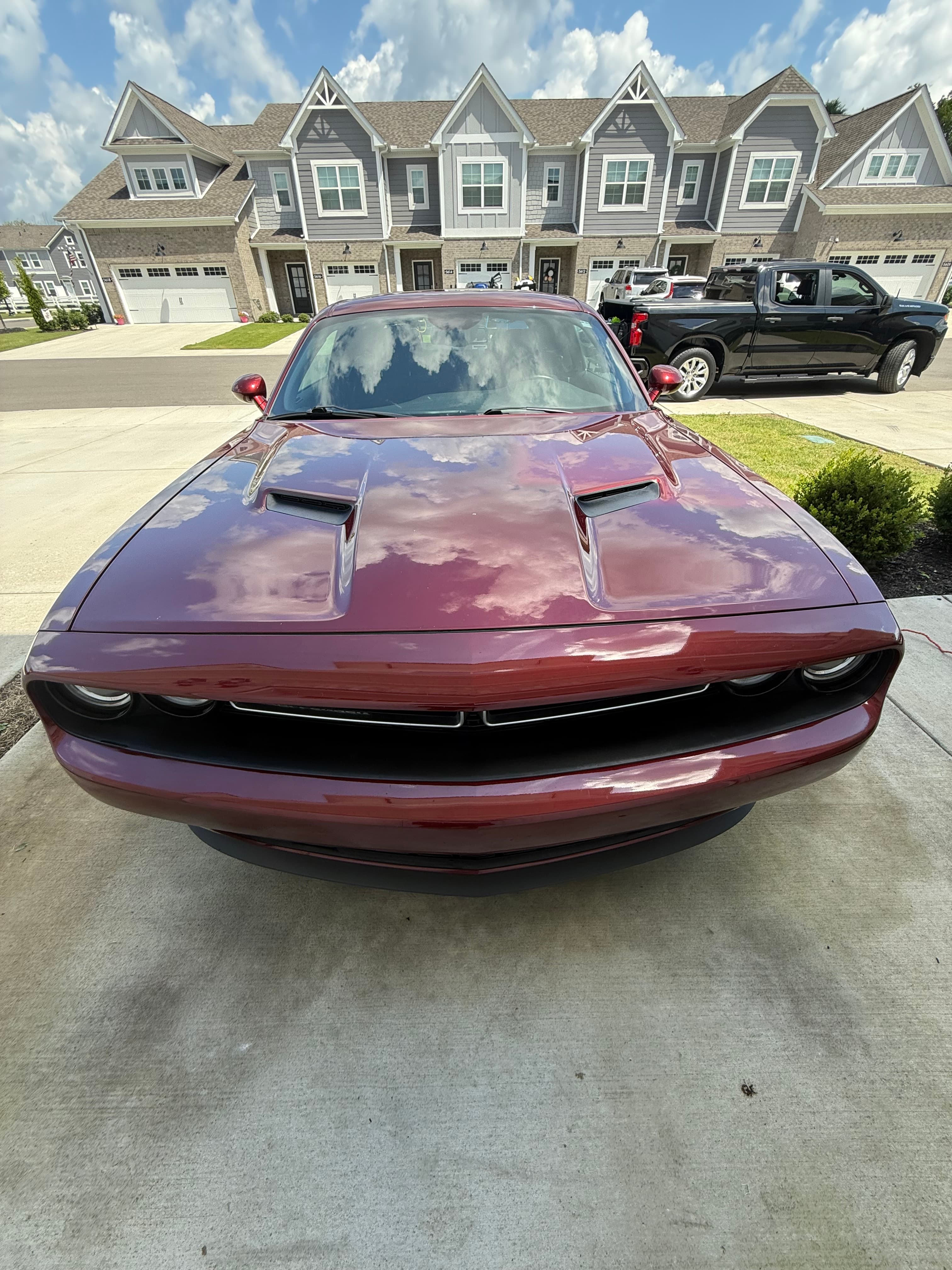 Maroon Dodge Challenger reflecting a cloudy sky on its hood, parked in a suburban driveway.