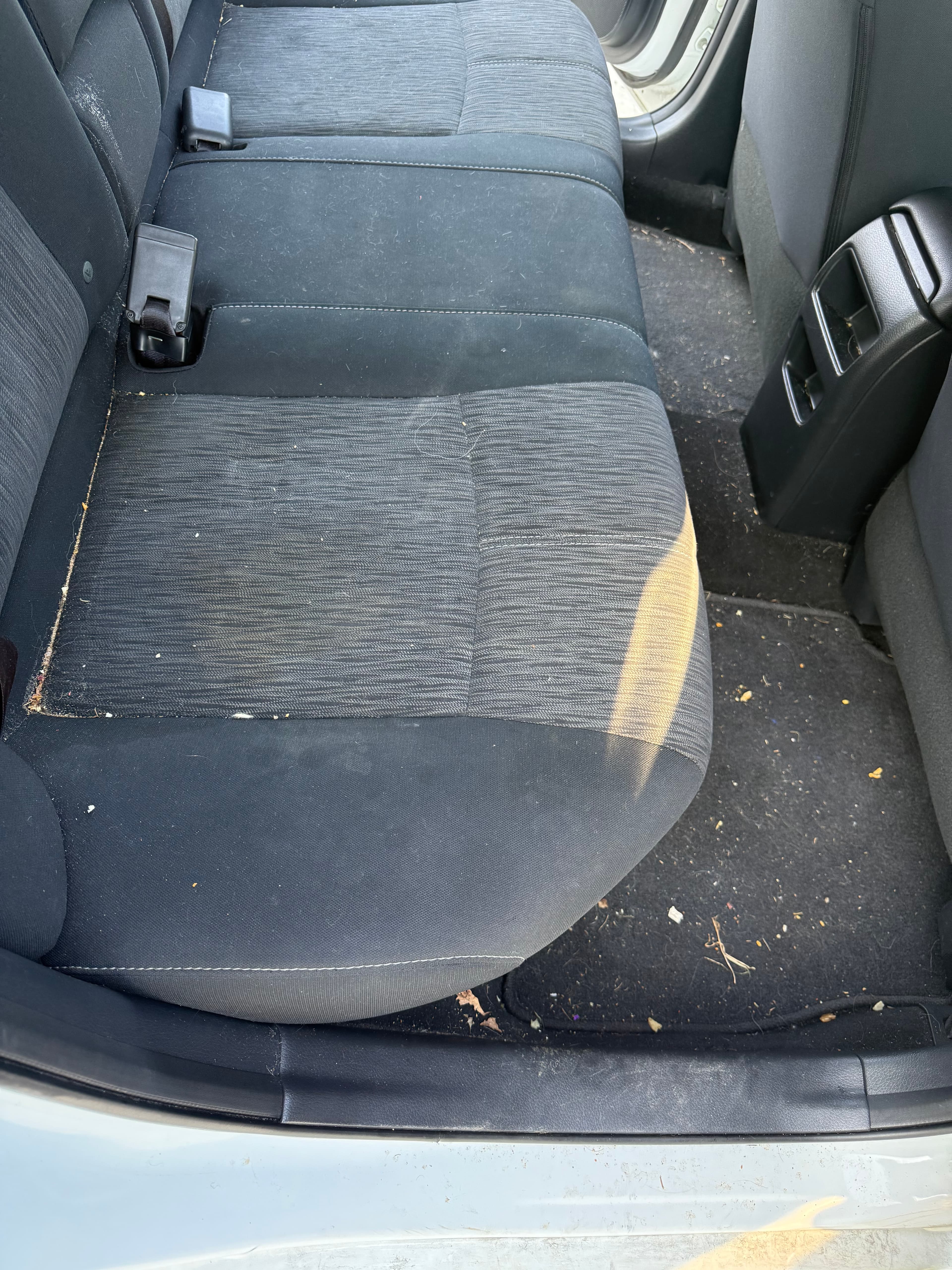 Dirty black fabric car back seat with crumbs and hair on the floor mat.
